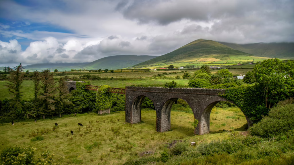 Historic viaduct amidst lush fields and mountains in Dingle, Ireland.